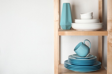 Photo of Shelving unit with set of dinnerware on light background, space for text. Interior element