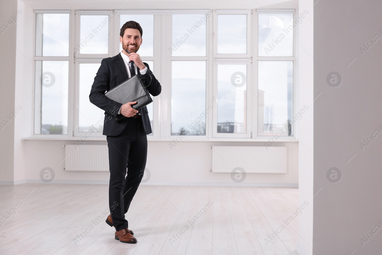 Photo of Happy real estate agent with leather portfolio in new apartment