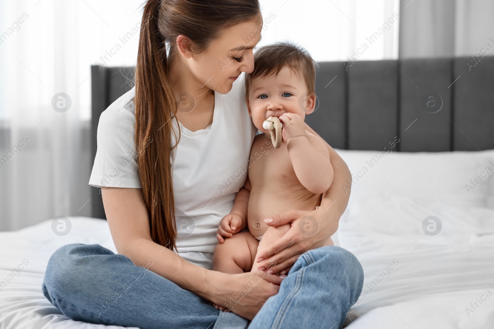 Photo of Happy mother sitting with her baby on bed at home