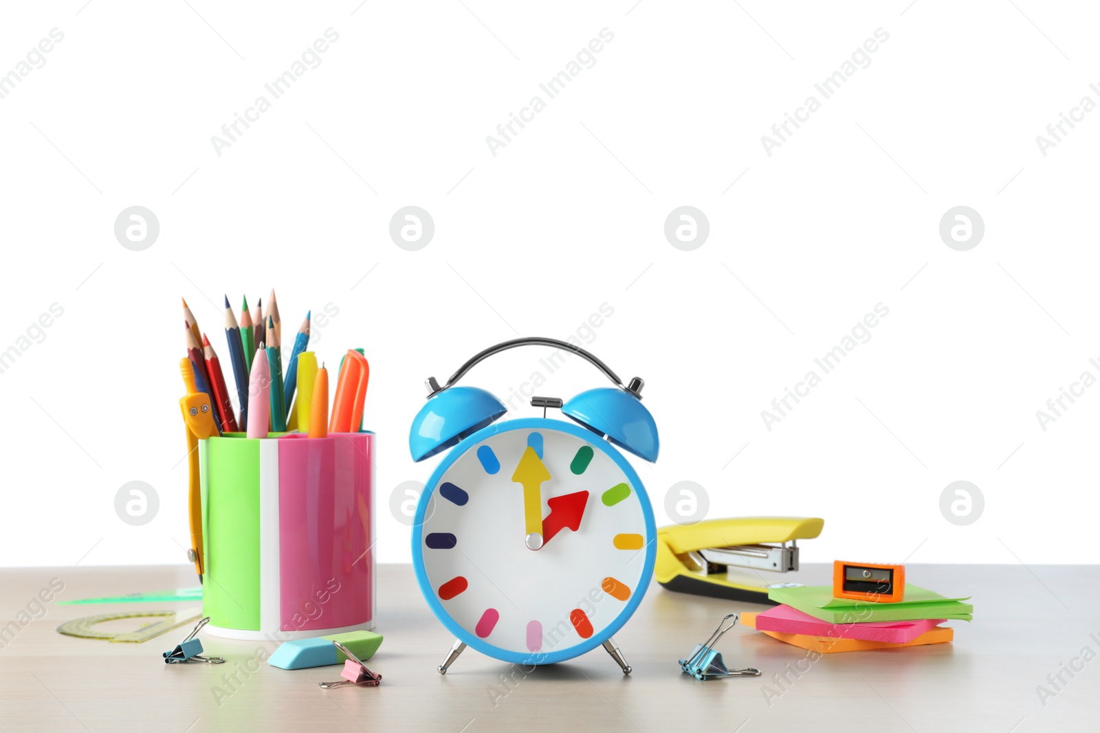 Photo of Light blue alarm clock and different stationery on wooden table against white background. School time