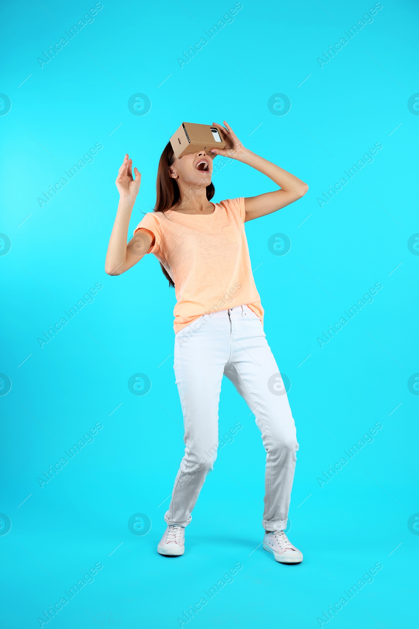 Photo of Young woman using cardboard virtual reality headset on color background