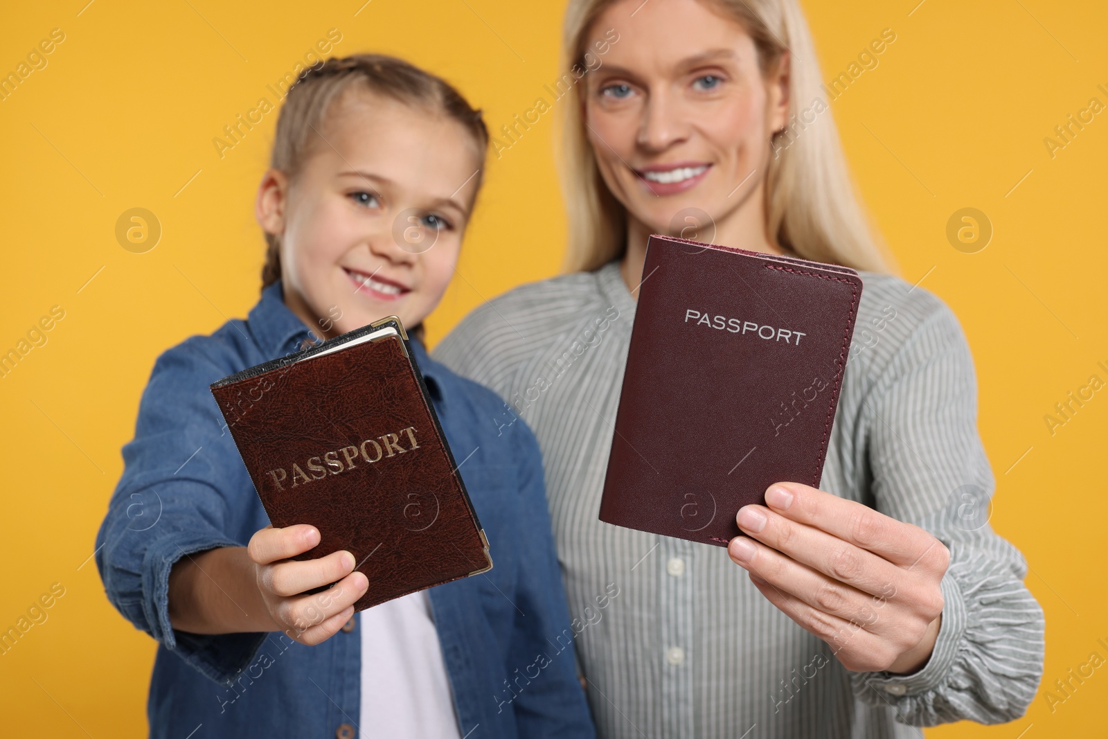 Photo of Immigration. Happy woman and her daughter with passports on orange background, selective focus