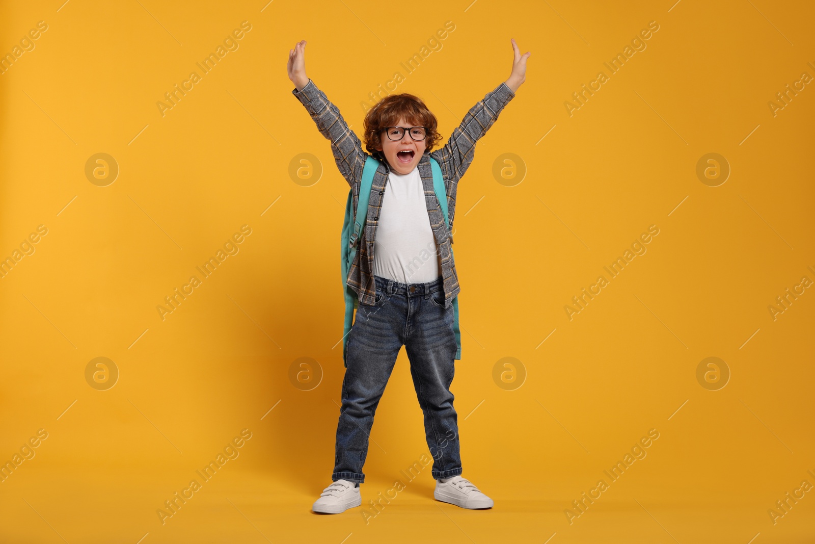 Photo of Emotional schoolboy with backpack on orange background