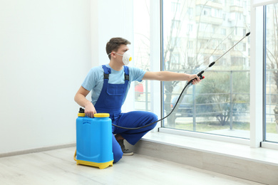 Photo of Pest control worker spraying pesticide near window indoors