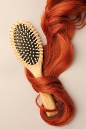 Photo of Wooden brush and red hair strand on light background, top view