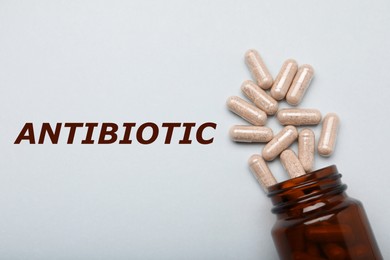 Image of Word Antibiotic, many gelatin capsules and bottle on light grey background, flat lay