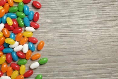 Delicious bright jelly beans on wooden background, top view. Space for text