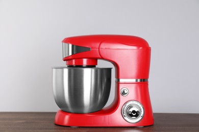 Photo of Modern red stand mixer on wooden table against gray background