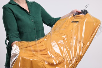 Dry-cleaning service. Woman holding dress in plastic bag on white background, closeup