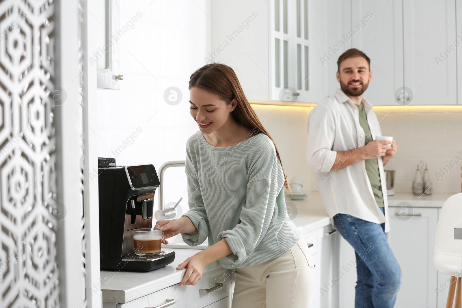 Photo of Happy couple preparing fresh aromatic coffee with modern machine in kitchen