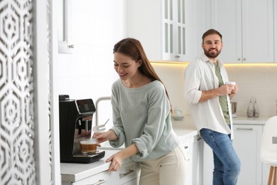 Happy couple preparing fresh aromatic coffee with modern machine in kitchen
