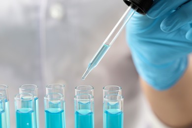 Scientist dripping liquid from pipette into test tube, closeup