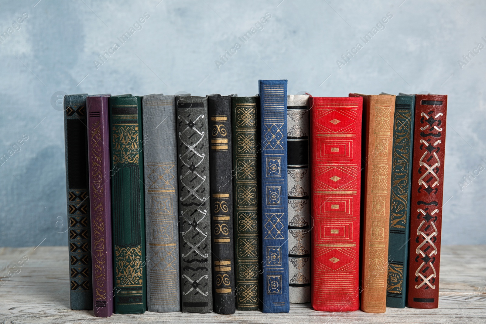 Photo of Stack of hardcover books on wooden table against light blue background