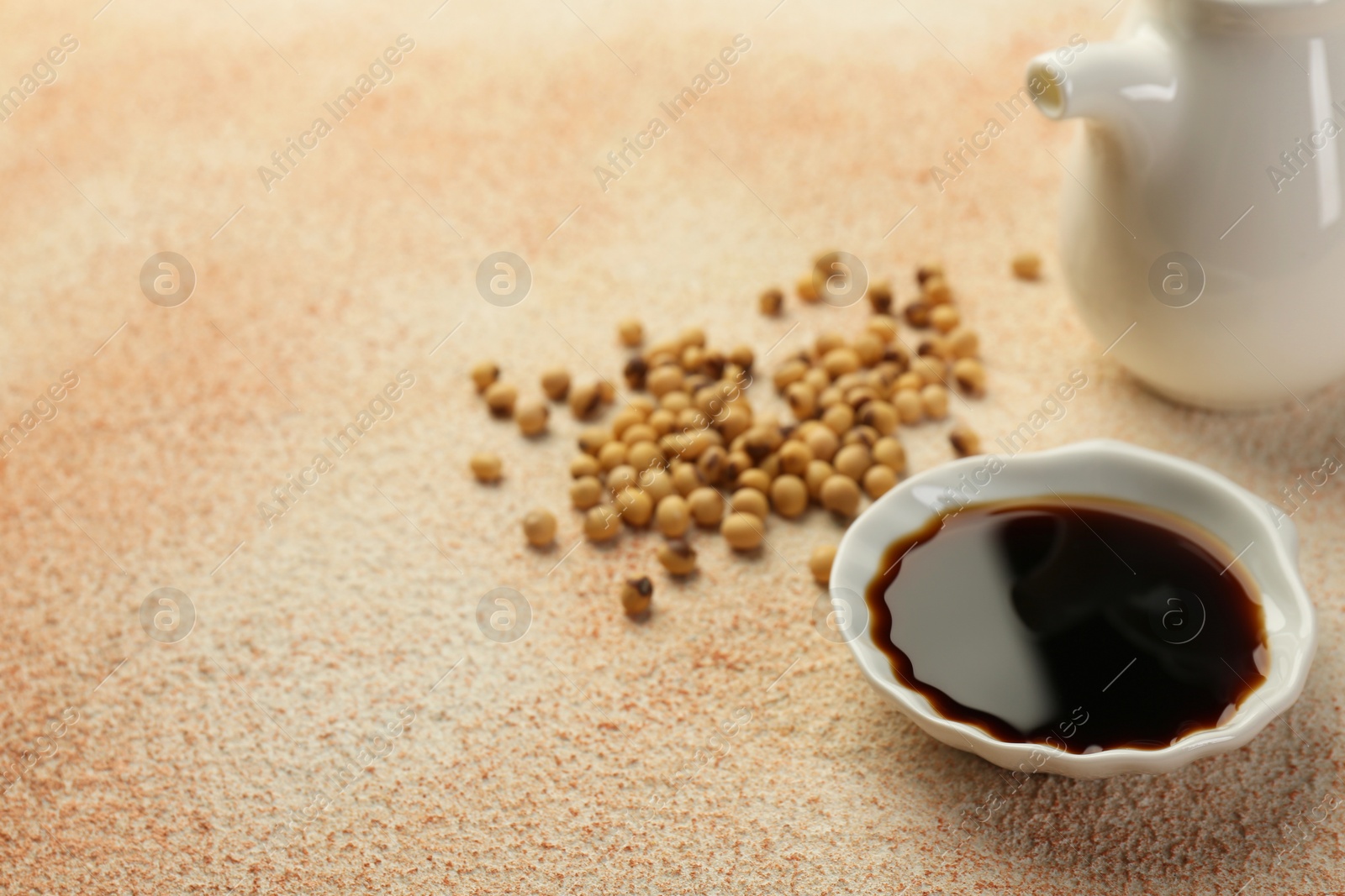 Photo of Soy sauce in bowl and beans on beige textured table. Space for text