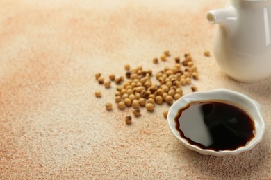 Soy sauce in bowl and beans on beige textured table. Space for text