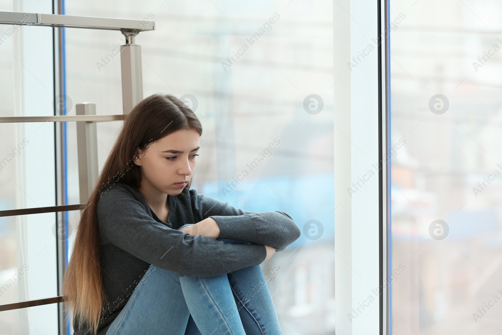 Photo of Upset teenage girl sitting at window indoors. Space for text