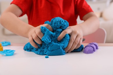 Little boy playing with bright kinetic sand at table indoors, closeup