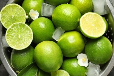 Photo of Colander with fresh ripe limes and ice cubes, closeup