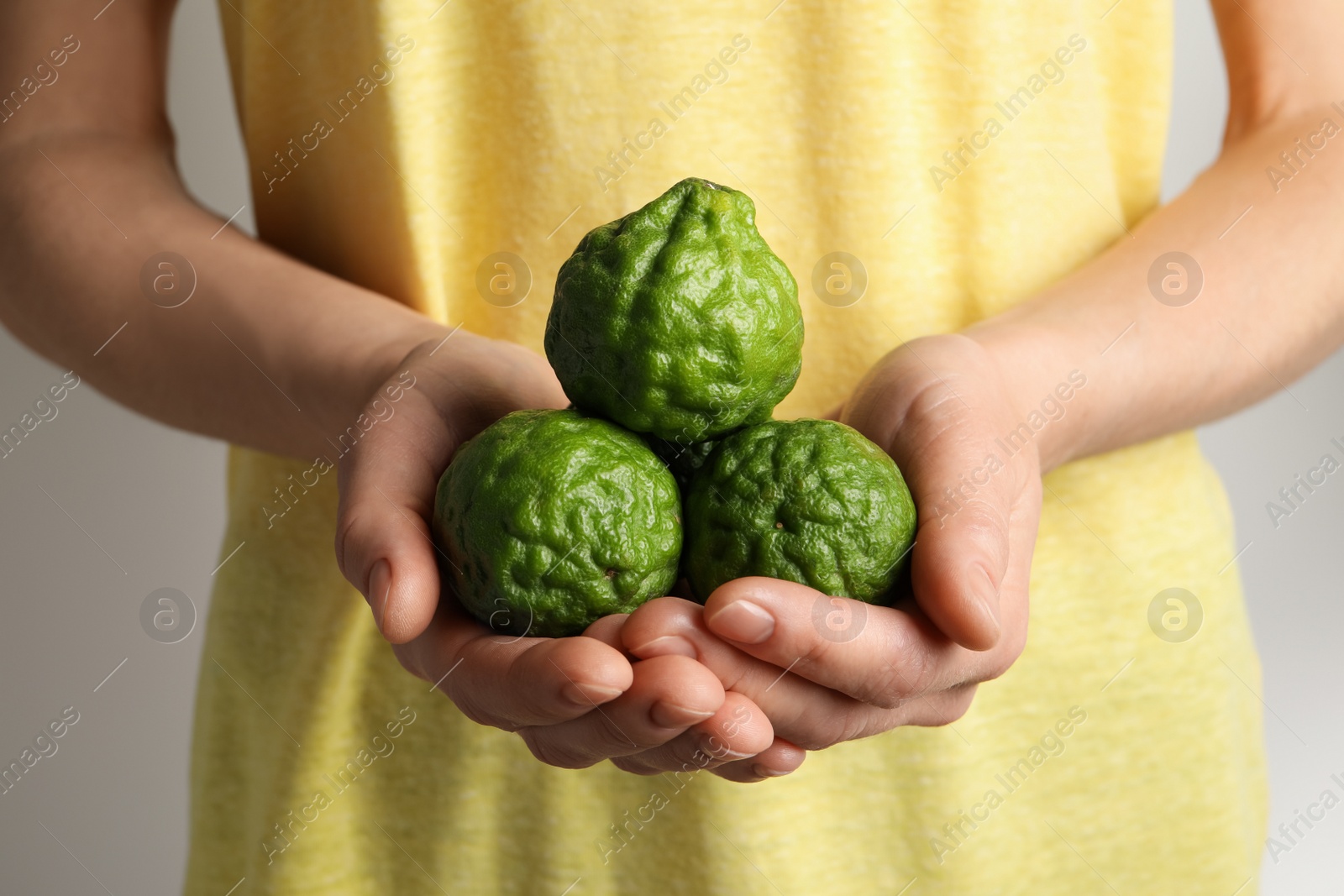 Photo of Woman holding pile of fresh ripe bergamot fruits on white background, closeup