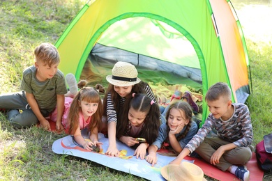 Photo of Little children with map near tent outdoors. Summer camp