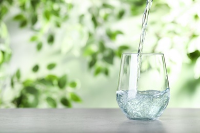 Pouring water into glass on grey table outdoors, space for text. Refreshing drink