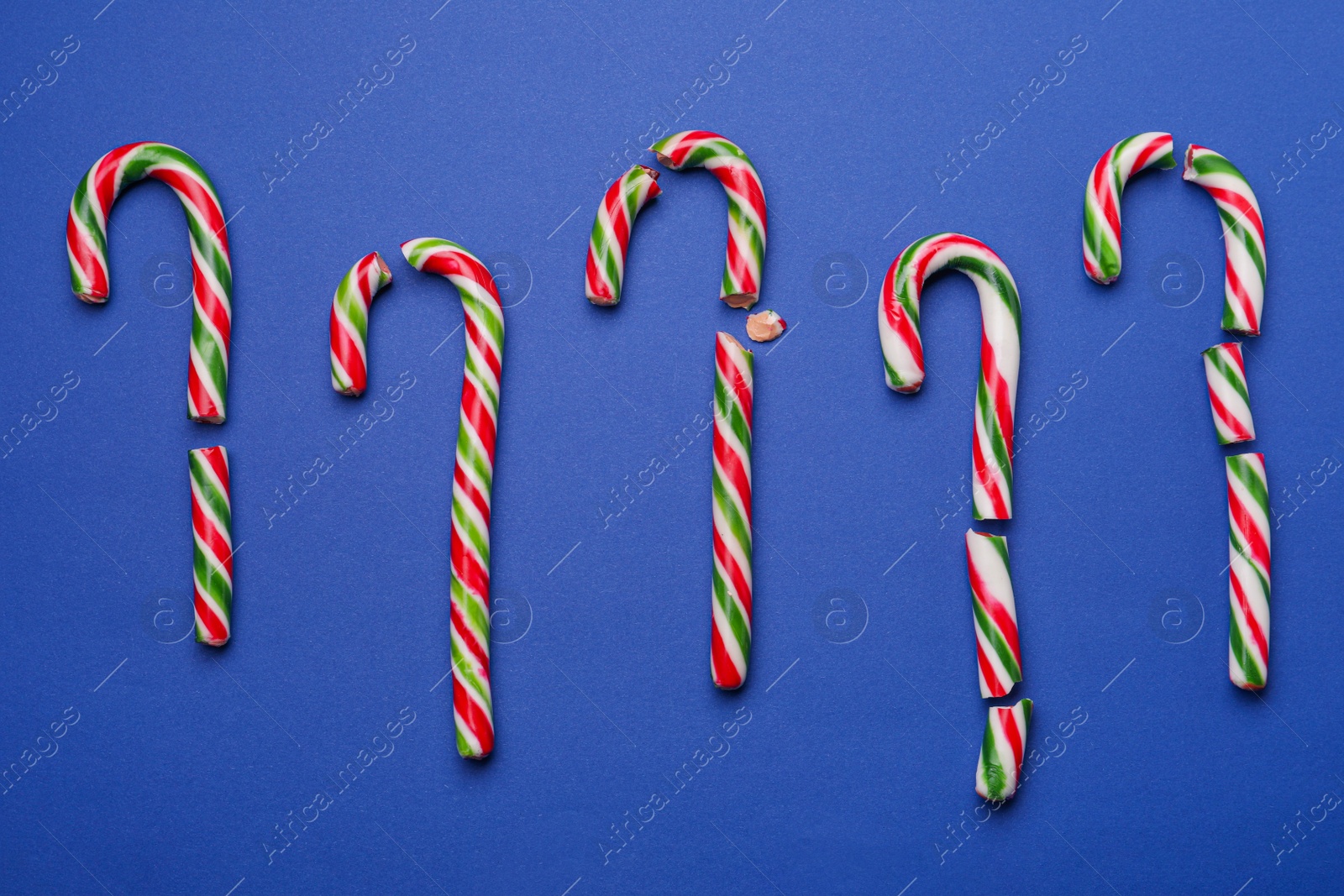 Photo of Broken sweet Christmas candy canes on blue background, flat lay