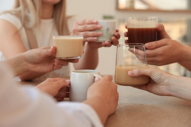 Photo of Friends drinking coffee at wooden table in cafe, closeup