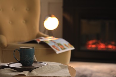 Photo of Cup of hot drink on table near fireplace at home, space for text. Cozy atmosphere