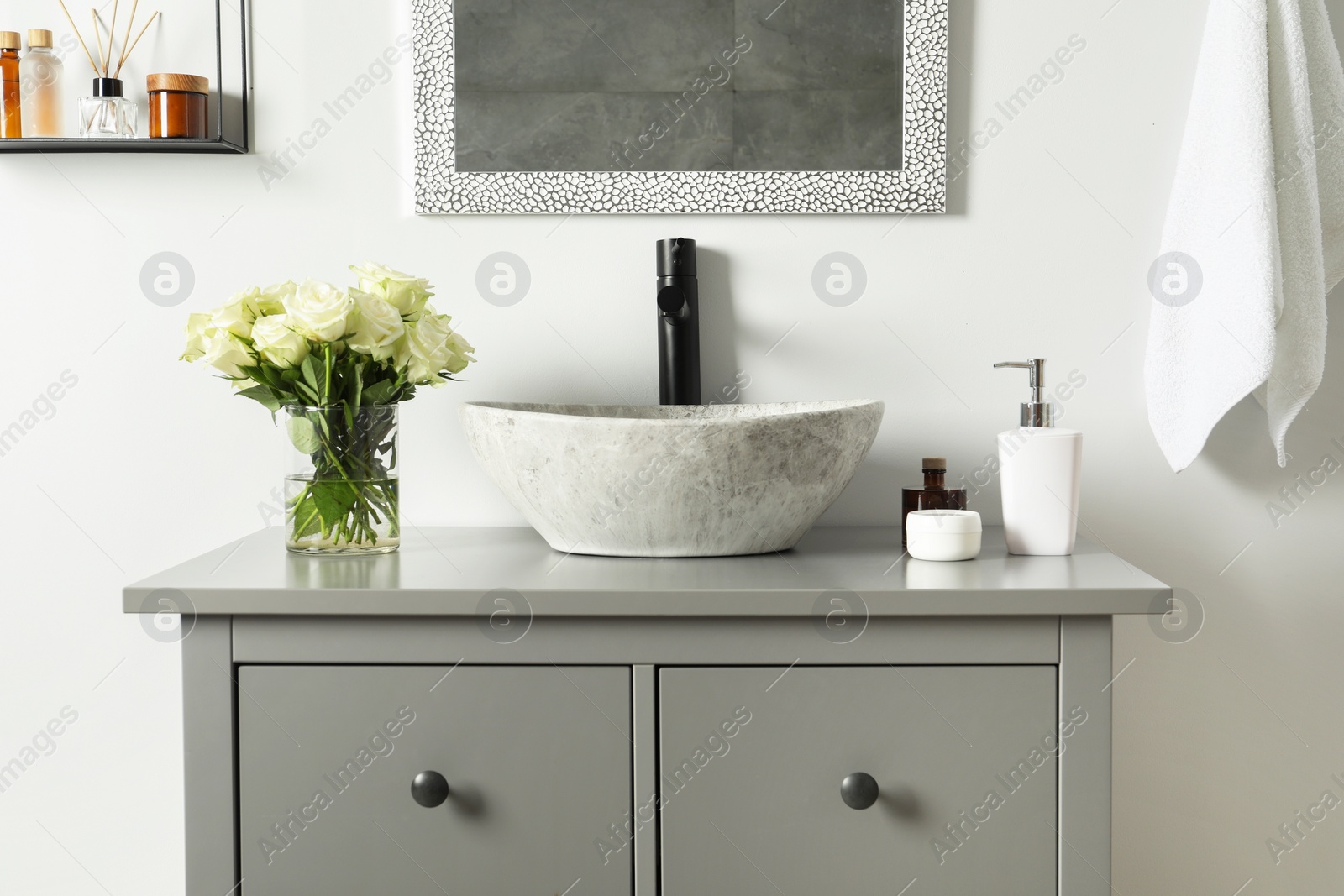 Photo of Vase with beautiful white roses and toiletries near sink in bathroom