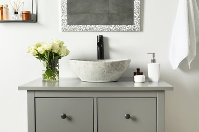 Vase with beautiful white roses and toiletries near sink in bathroom