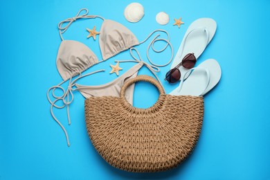 Stylish bag with beach accessories on light blue background, flat lay