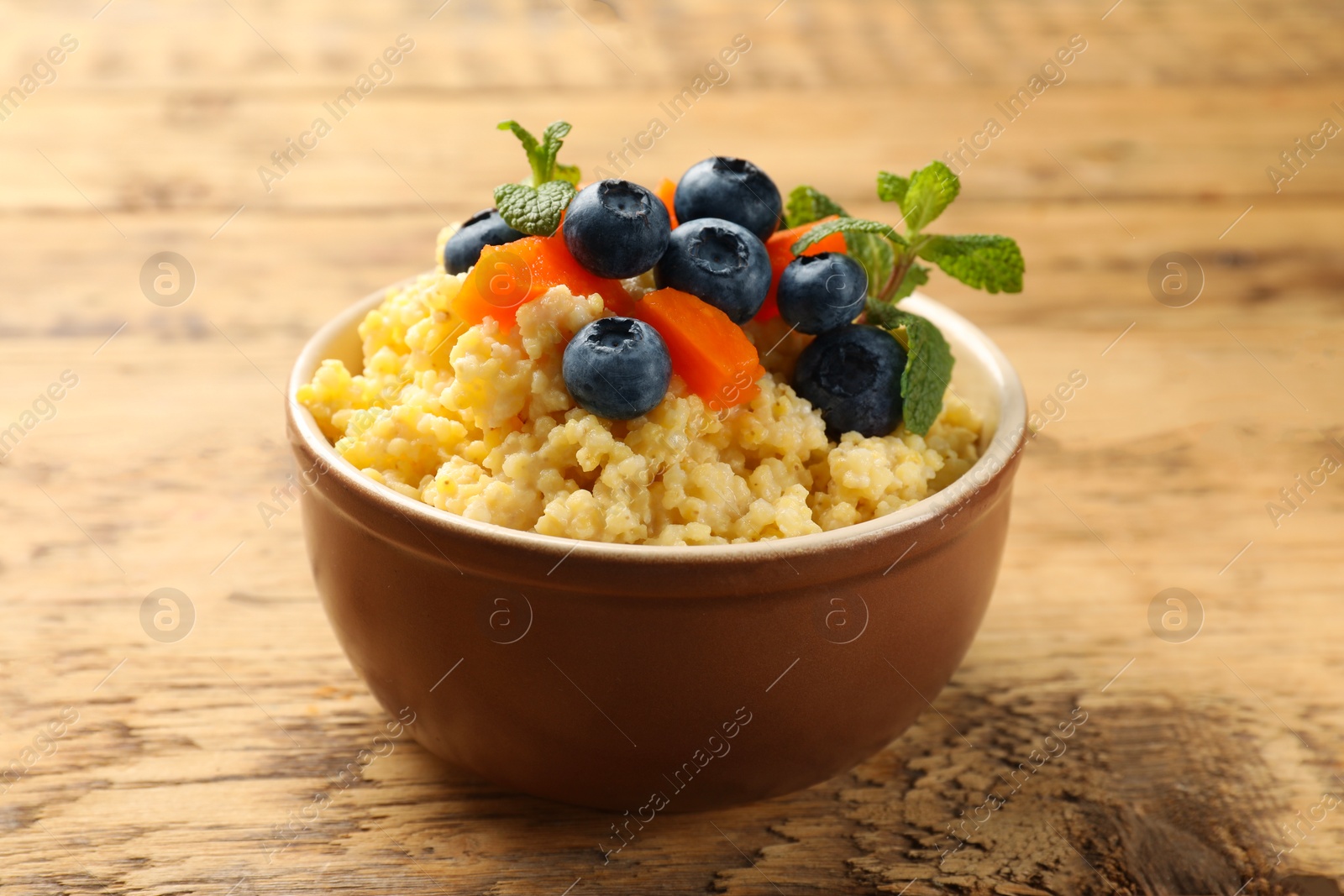 Photo of Tasty millet porridge with blueberries, pumpkin and mint in bowl on wooden table, closeup