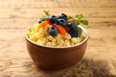 Tasty millet porridge with blueberries, pumpkin and mint in bowl on wooden table, closeup