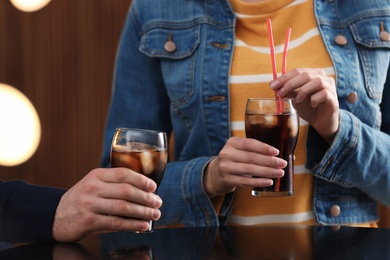 People holding glasses of cola with ice on blurred background, closeup