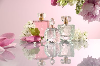 Luxury perfumes and floral decor on mirror surface against pink background