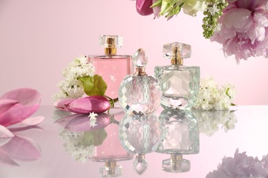 Photo of Luxury perfumes and floral decor on mirror surface against pink background