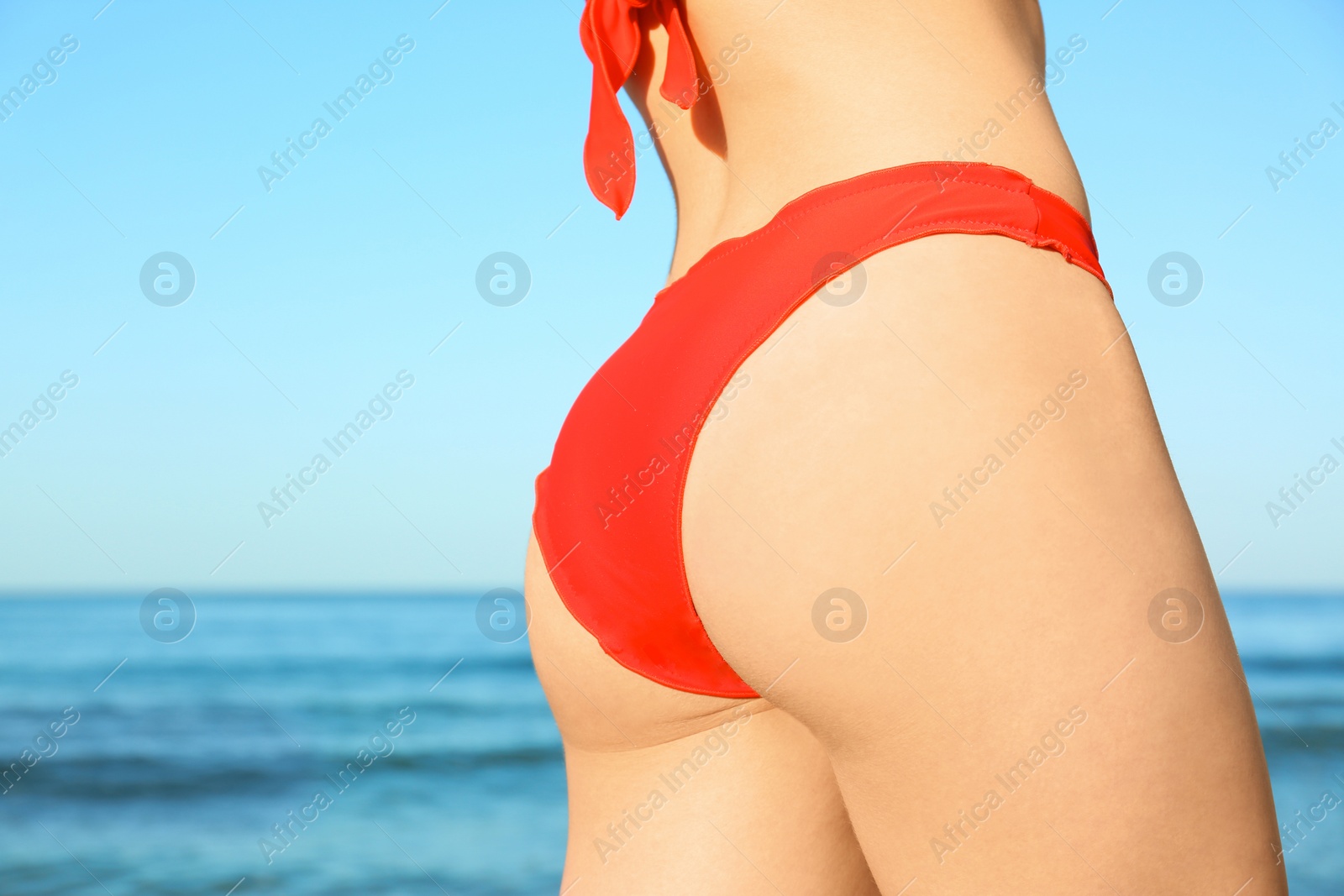 Photo of Young woman in red bikini near sea, closeup. Space for text