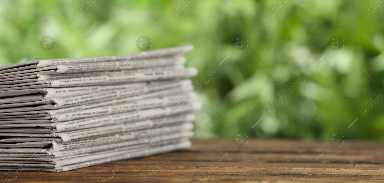 Photo of Stack of newspapers on wooden table against blurred green background, space for text. Journalist's work