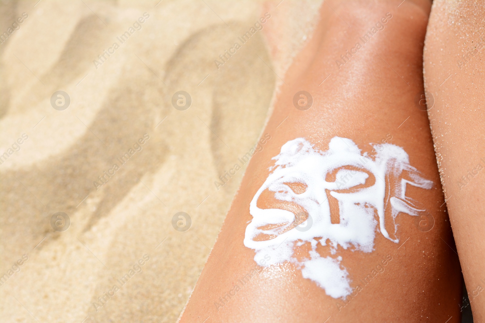 Photo of Woman with abbreviation SPF of sunscreen on leg at beach, closeup. Space for text