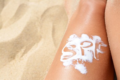 Woman with abbreviation SPF of sunscreen on leg at beach, closeup. Space for text