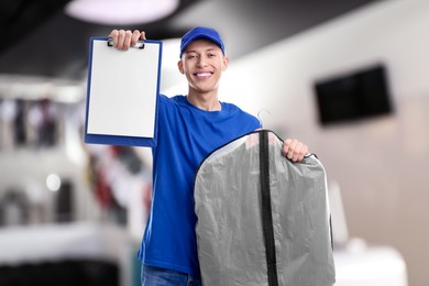 Image of Happy courier with garment cover of clothes showing clipboard in dry-cleaning