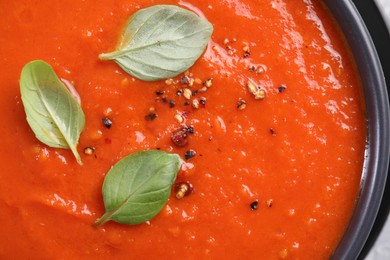 Photo of Delicious tomato cream soup with basil and ground pepper in bowl, top view