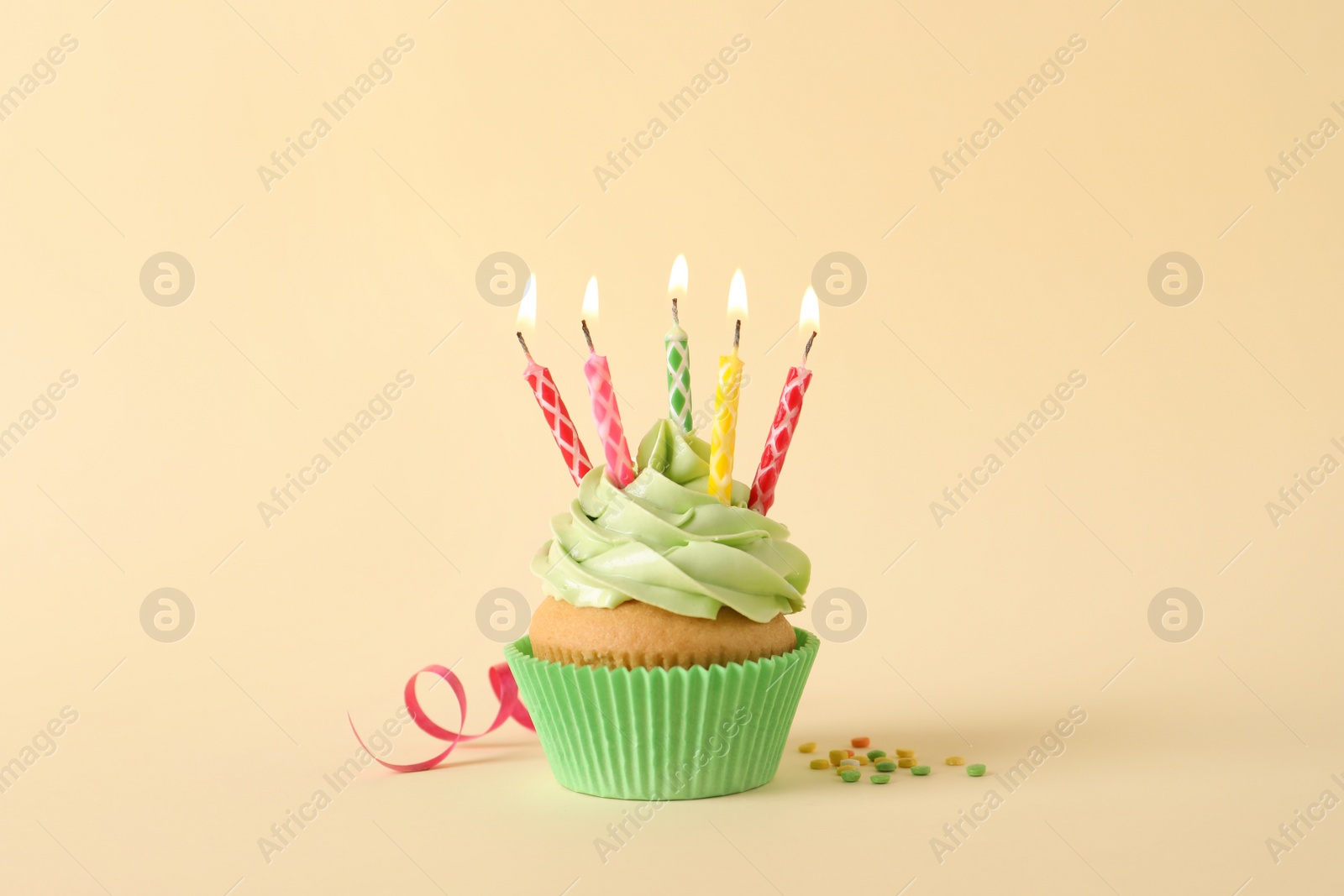 Photo of Birthday cupcake with burning candles, streamer and sprinkles on beige background