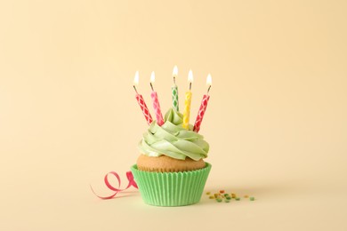 Birthday cupcake with burning candles, streamer and sprinkles on beige background