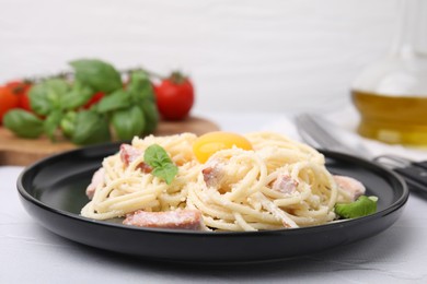 Plate of tasty pasta Carbonara with basil leaves and egg yolk on white textured table, closeup