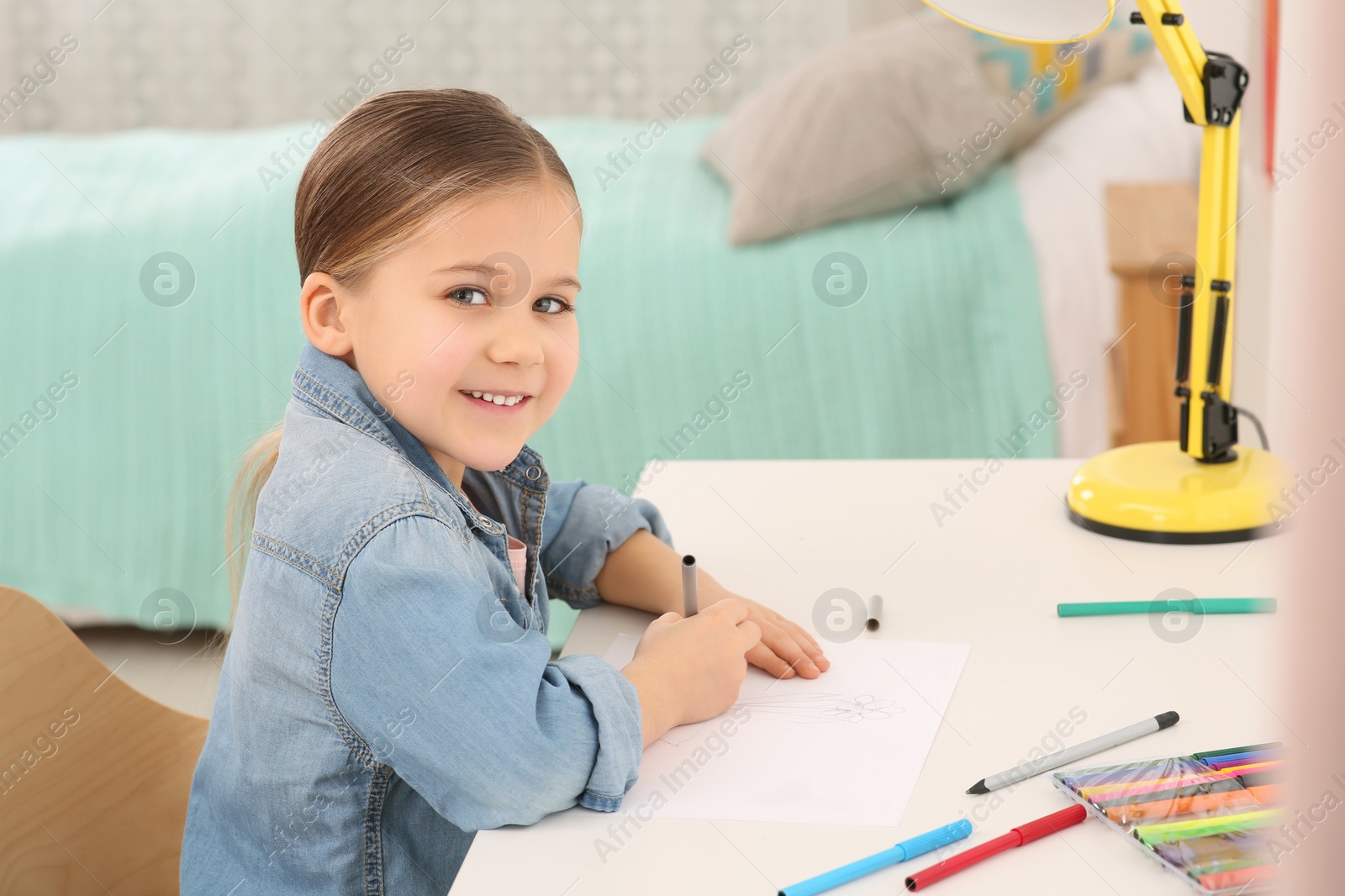 Photo of Cute little girl drawing with marker at desk in room. Home workplace