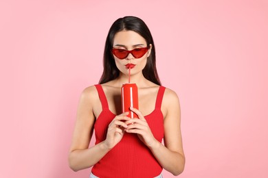 Photo of Beautiful young woman with stylish sunglasses drinking from tin can on pink background