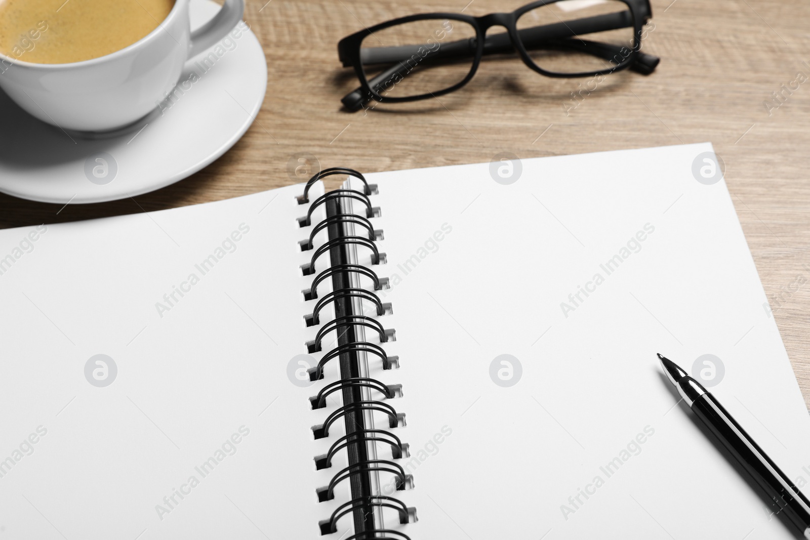 Photo of Empty notebook, coffee, glasses and pen on wooden table, closeup
