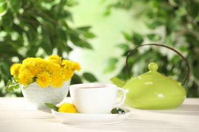 Photo of Delicious fresh tea and dandelion flowers on white table against blurred background