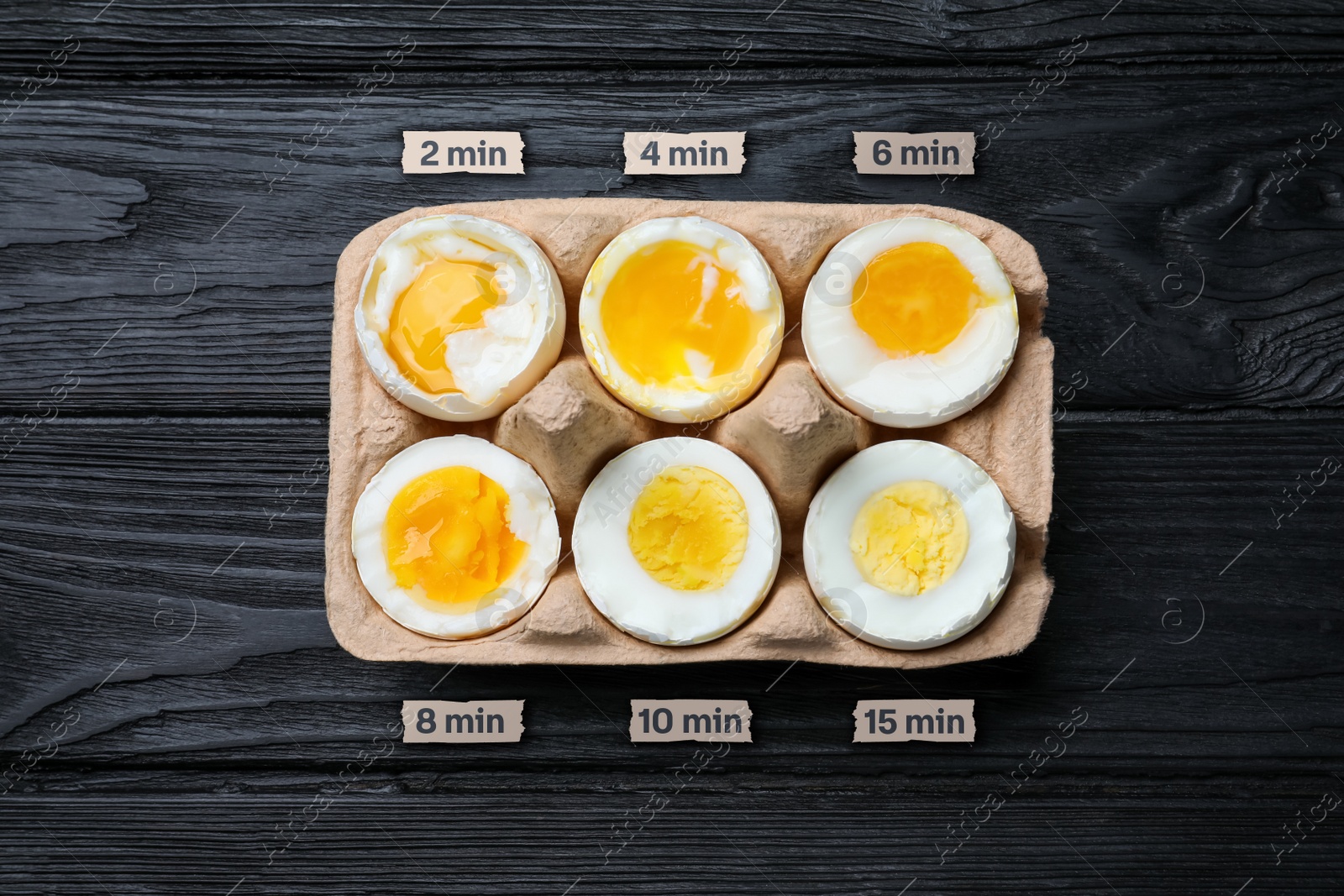 Image of Boiled chicken eggs of different readiness stages in carton on black wooden table, top view